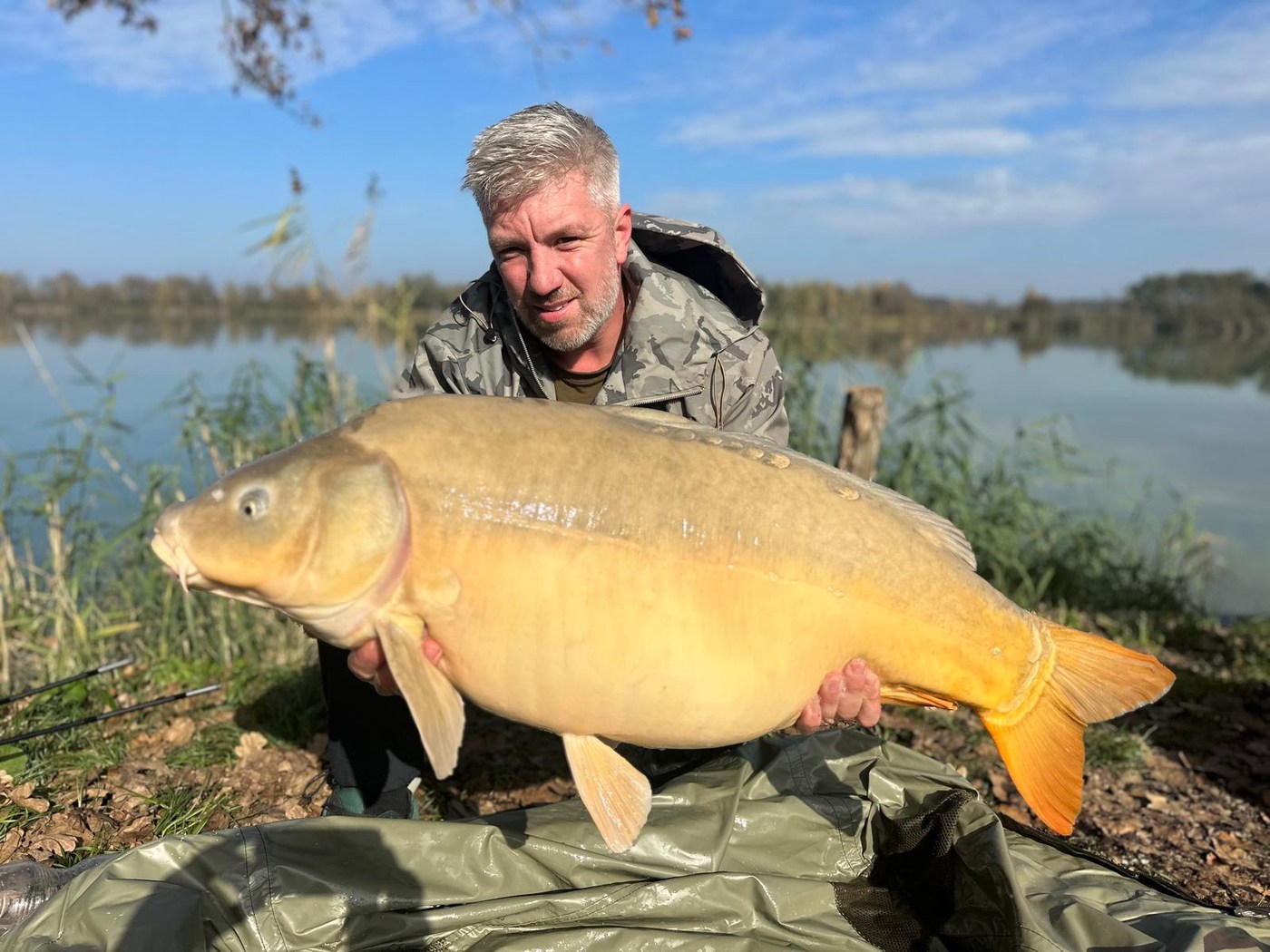 Rob Fisher, founder of Tackle Taxi, holding a large mirror carp at the lakeside